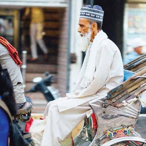 A person in a white robe and hat sitting in a rickshaw

Description automatically generated