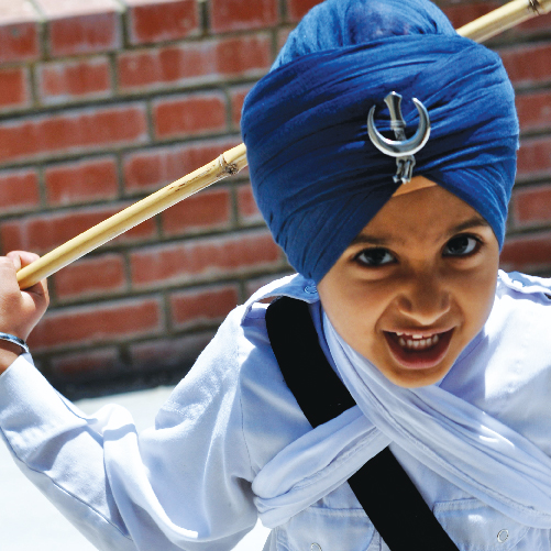 A young child wearing a turban and holding a stick

Description automatically generated