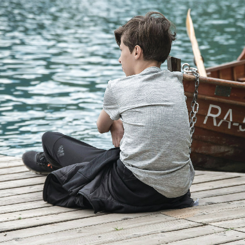 A child sitting on a dock next to a boat

Description automatically generated