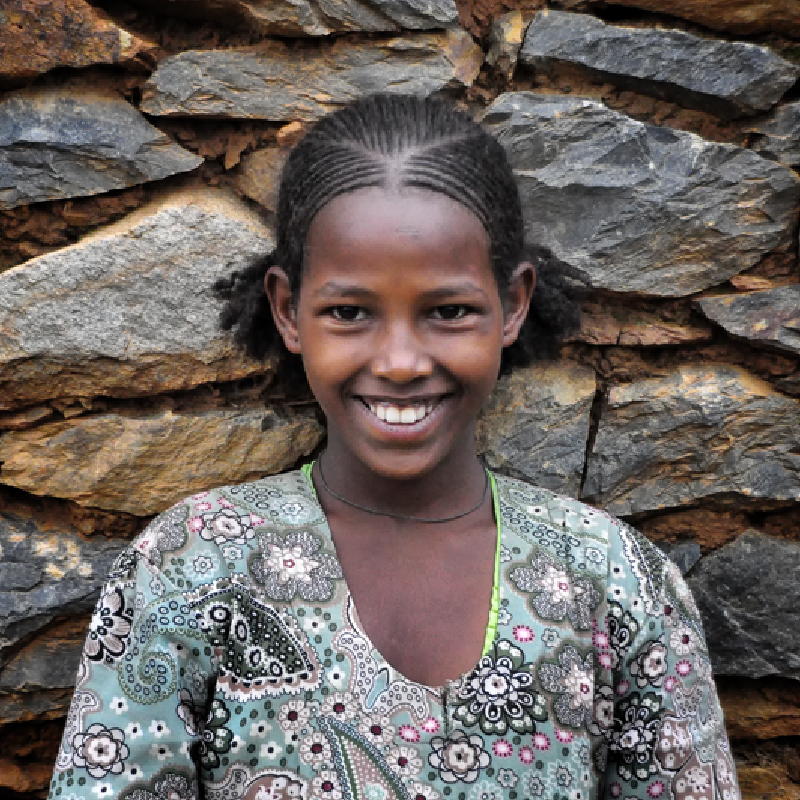 A young child smiling in front of a stone wall
Description automatically generated